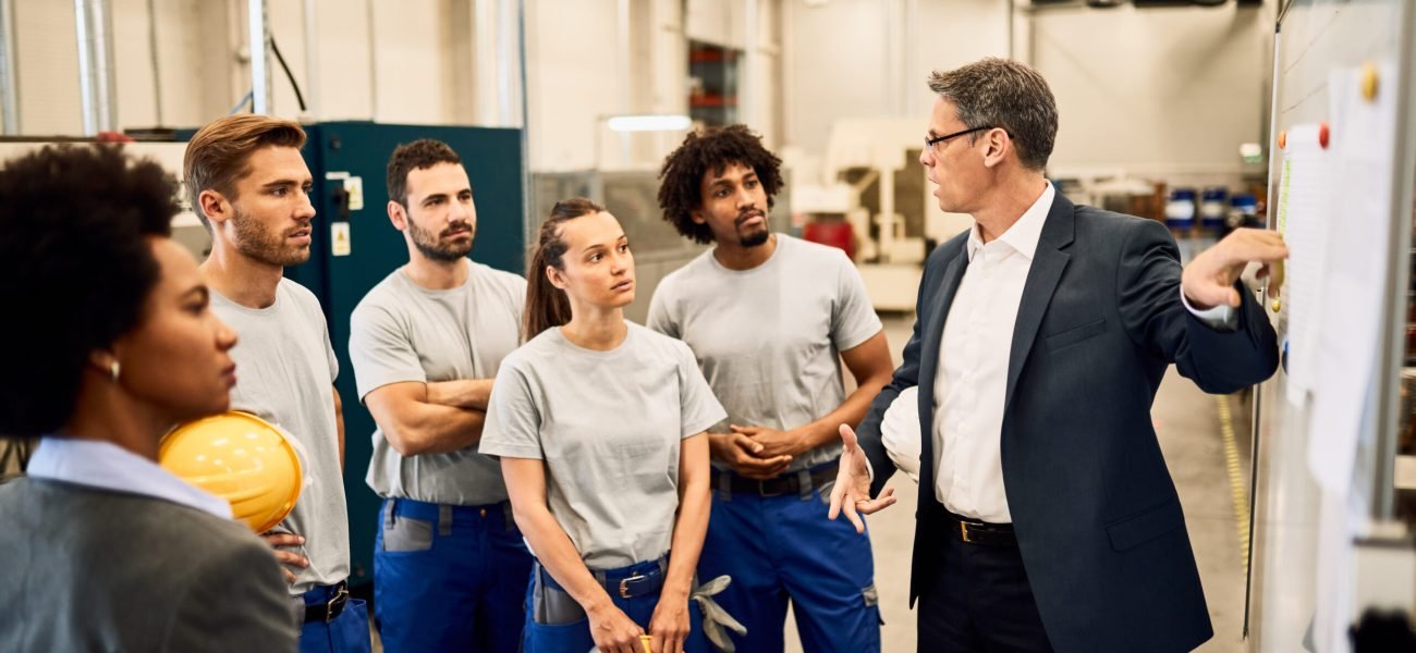 Mid adult businessman giving presentation to group of industrial workers in a factory.
